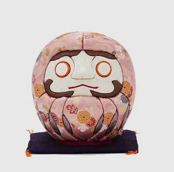Large pink kimekomi daruma doll on a purple cushion
