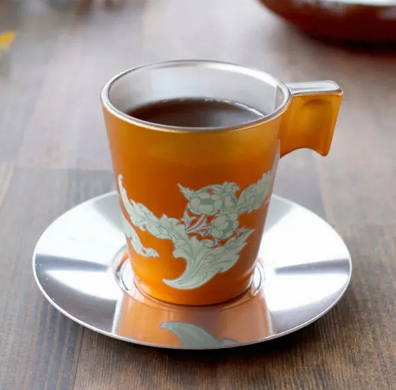 Orange cup and steel saucer with a pale floral pattern and coffee inside