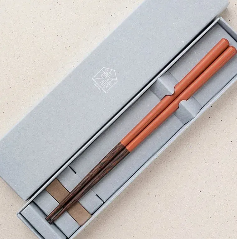 Pair of orange and dark chopsticks in a grey gift box